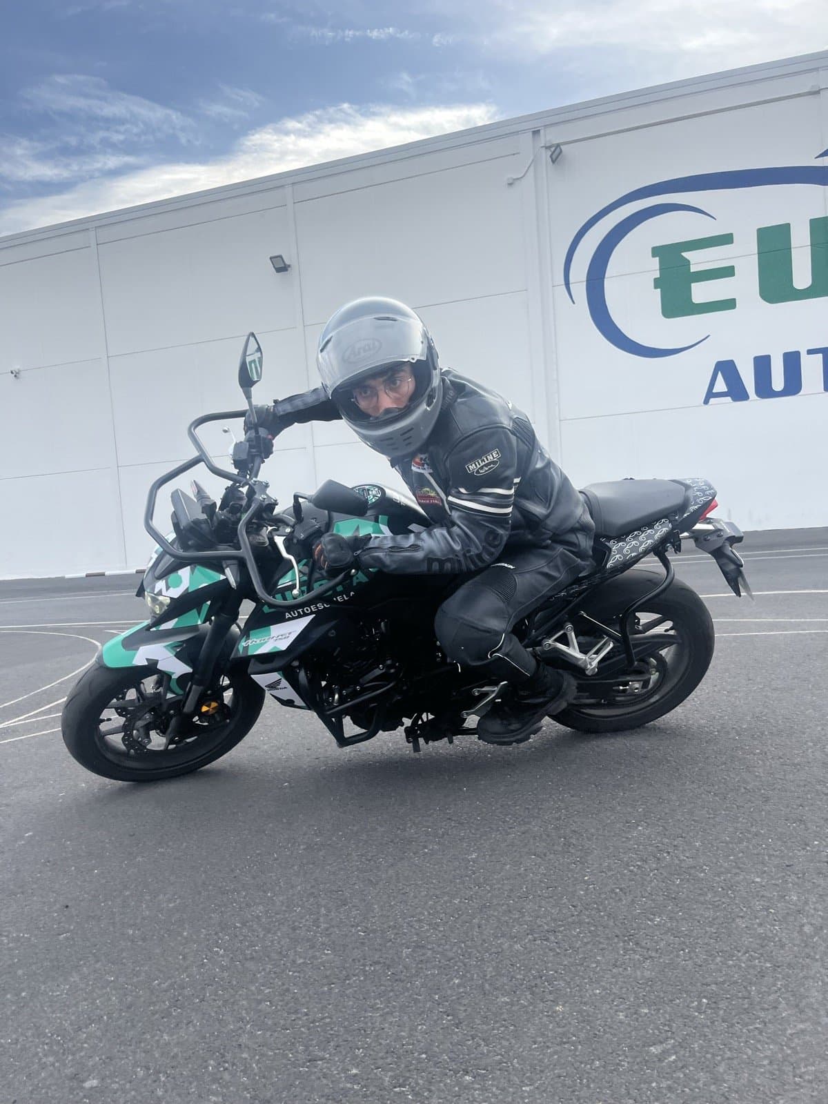 Alumno sobre la moto de Autoescuela Europa junto al logo, en Granada